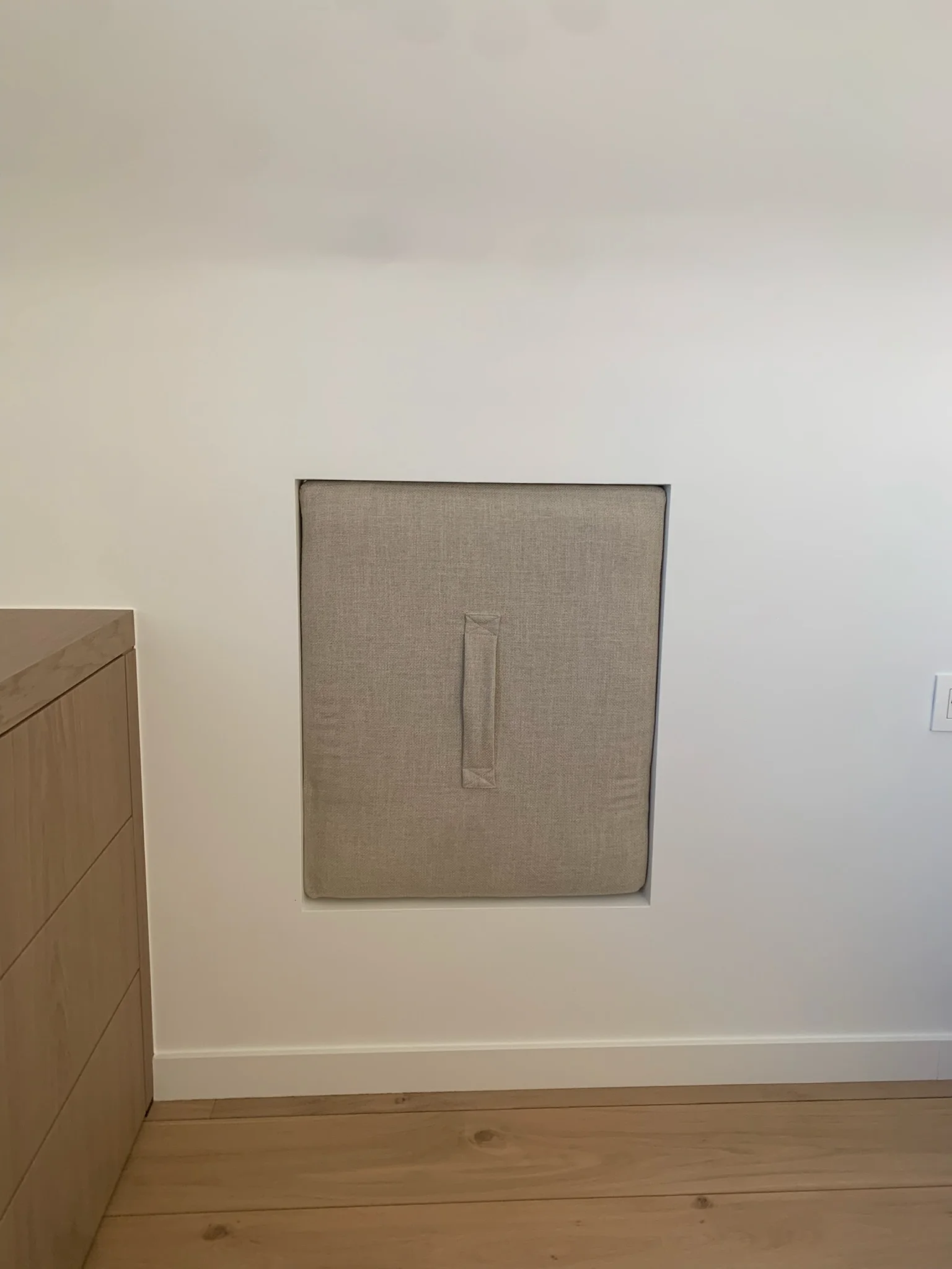 Beige stoffen paneel met handgreep in een muurnis, in een minimalistisch interieur met houten vloer
