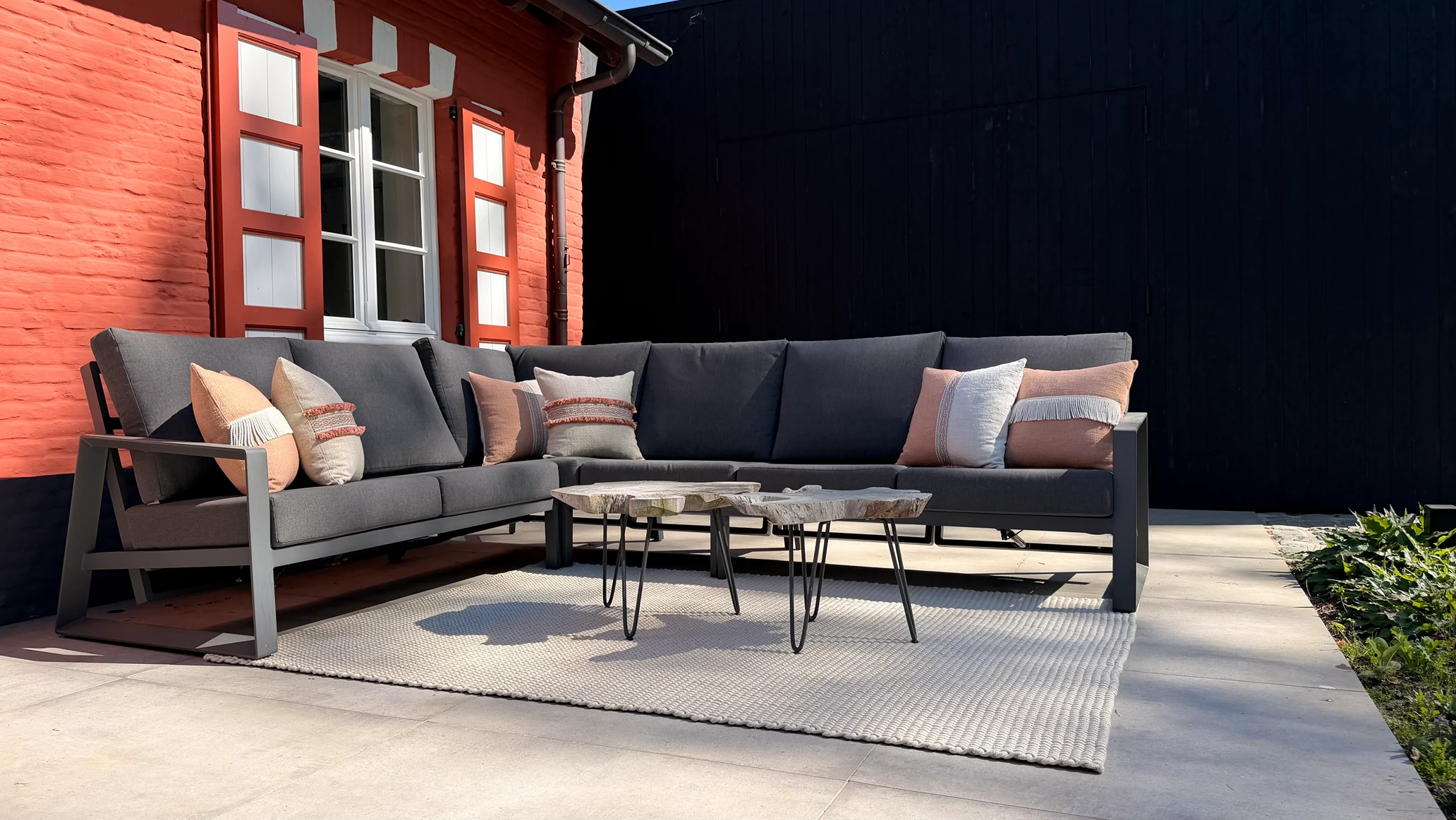 Antracietgrijze buitenlounge hoekbank met terracotta en beige sierkussens op een geweven buitenkleed