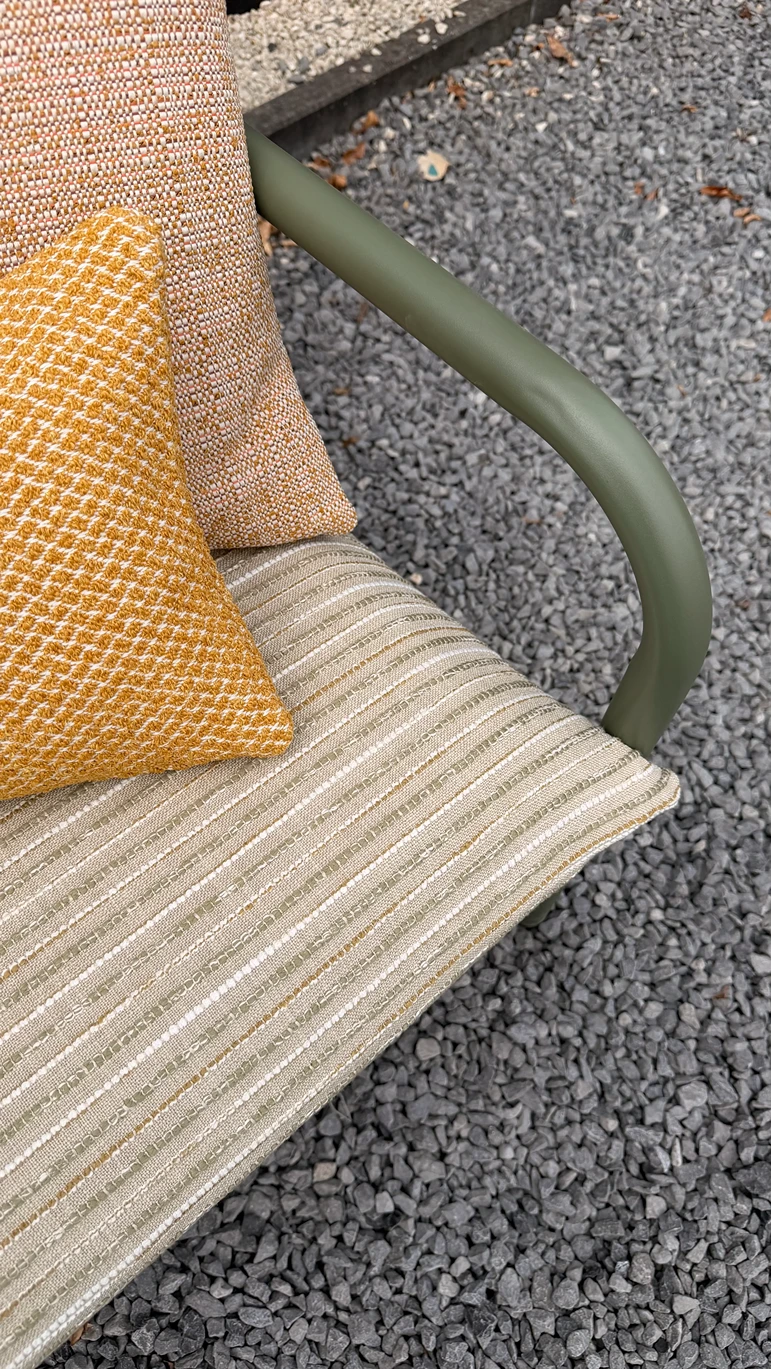 Close-up van de armleuning van een olijfgroene buitenfauteuil met okergele en beige sierkussens