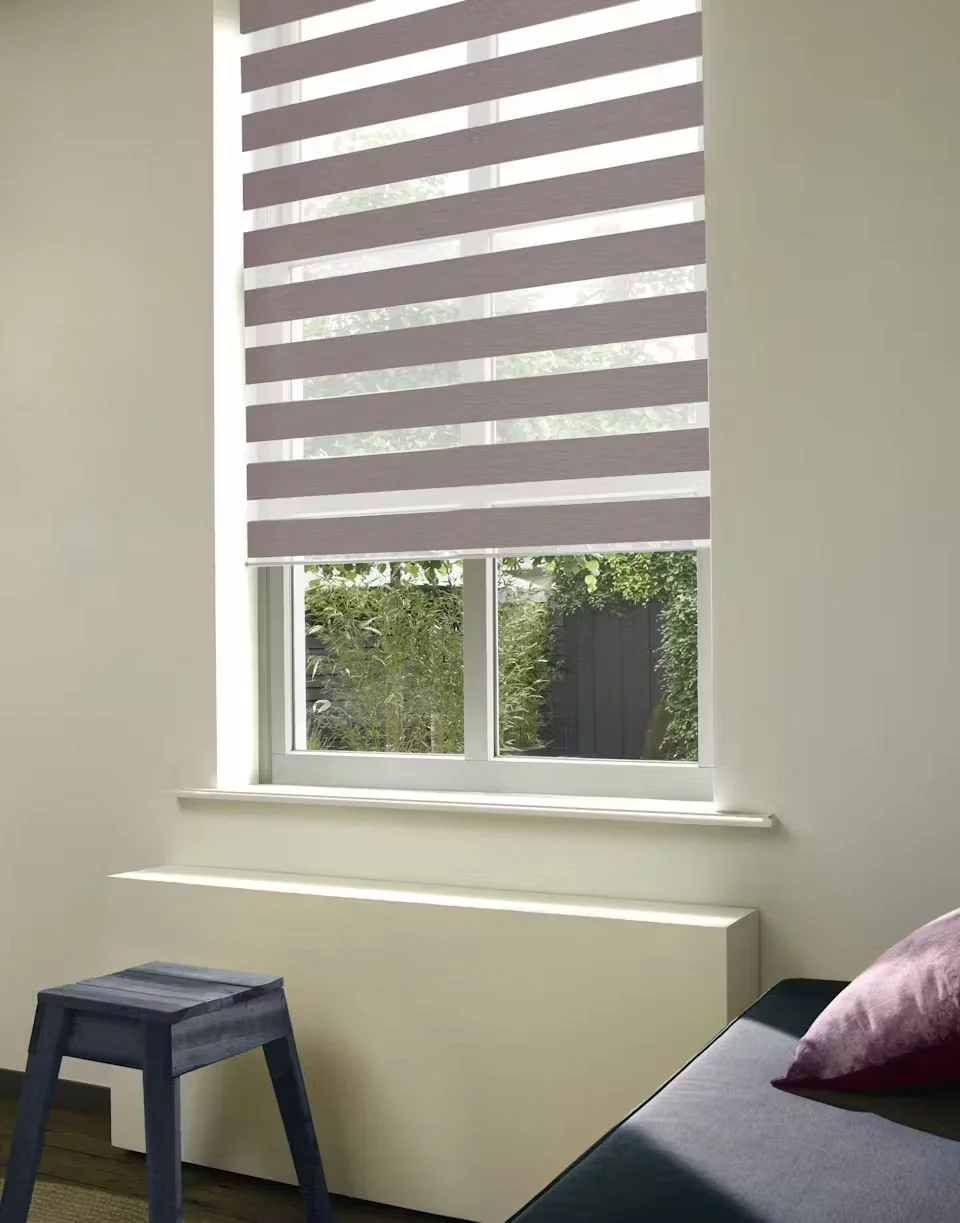 Duo-rolgordijn in taupe en wit voor een raam boven een radiatorombouw met zicht op de tuin