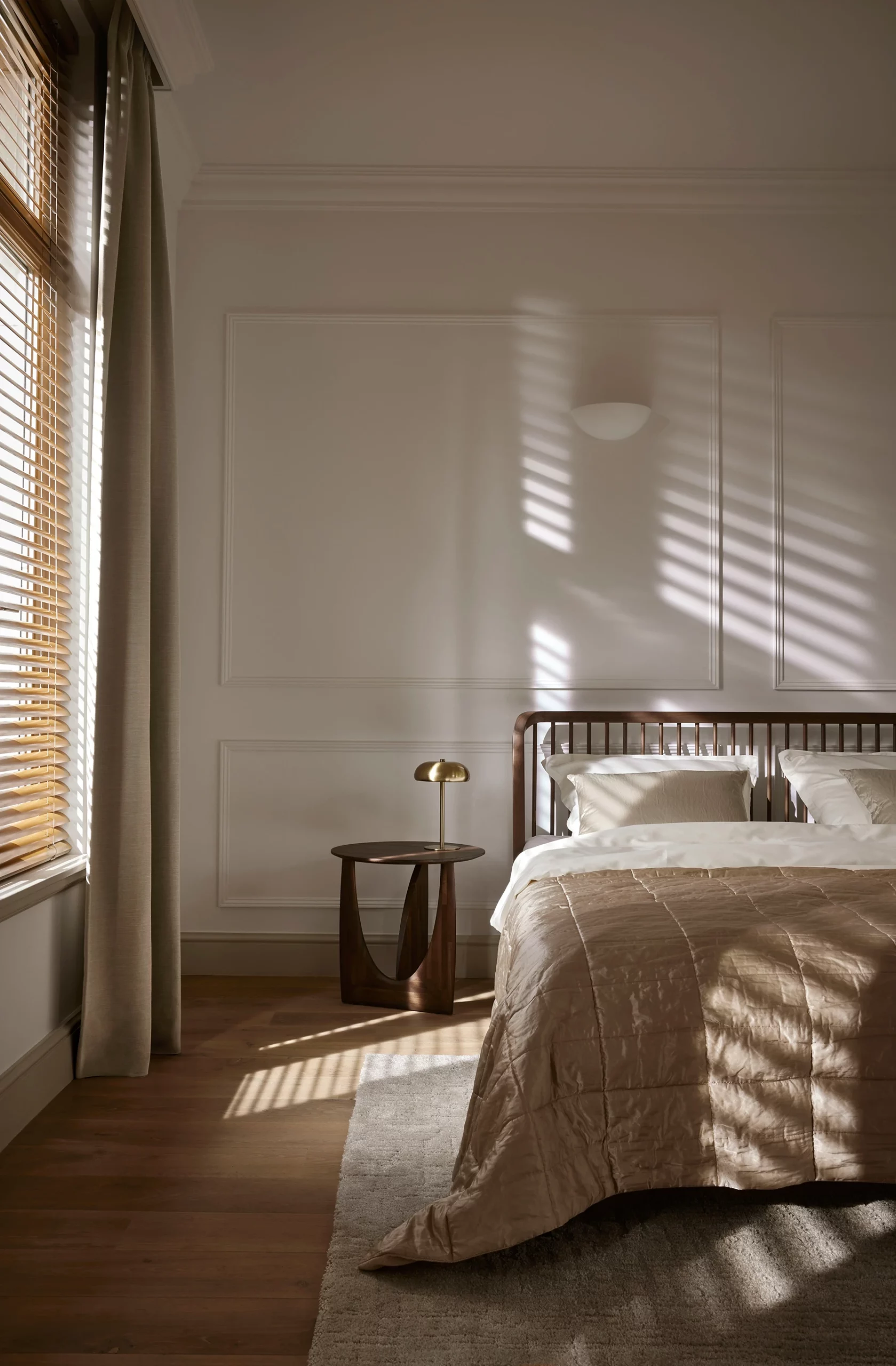Houten jaloezieën met schaduwpatroon op de muur in een klassieke slaapkamer met houten bed en beige beddengoed