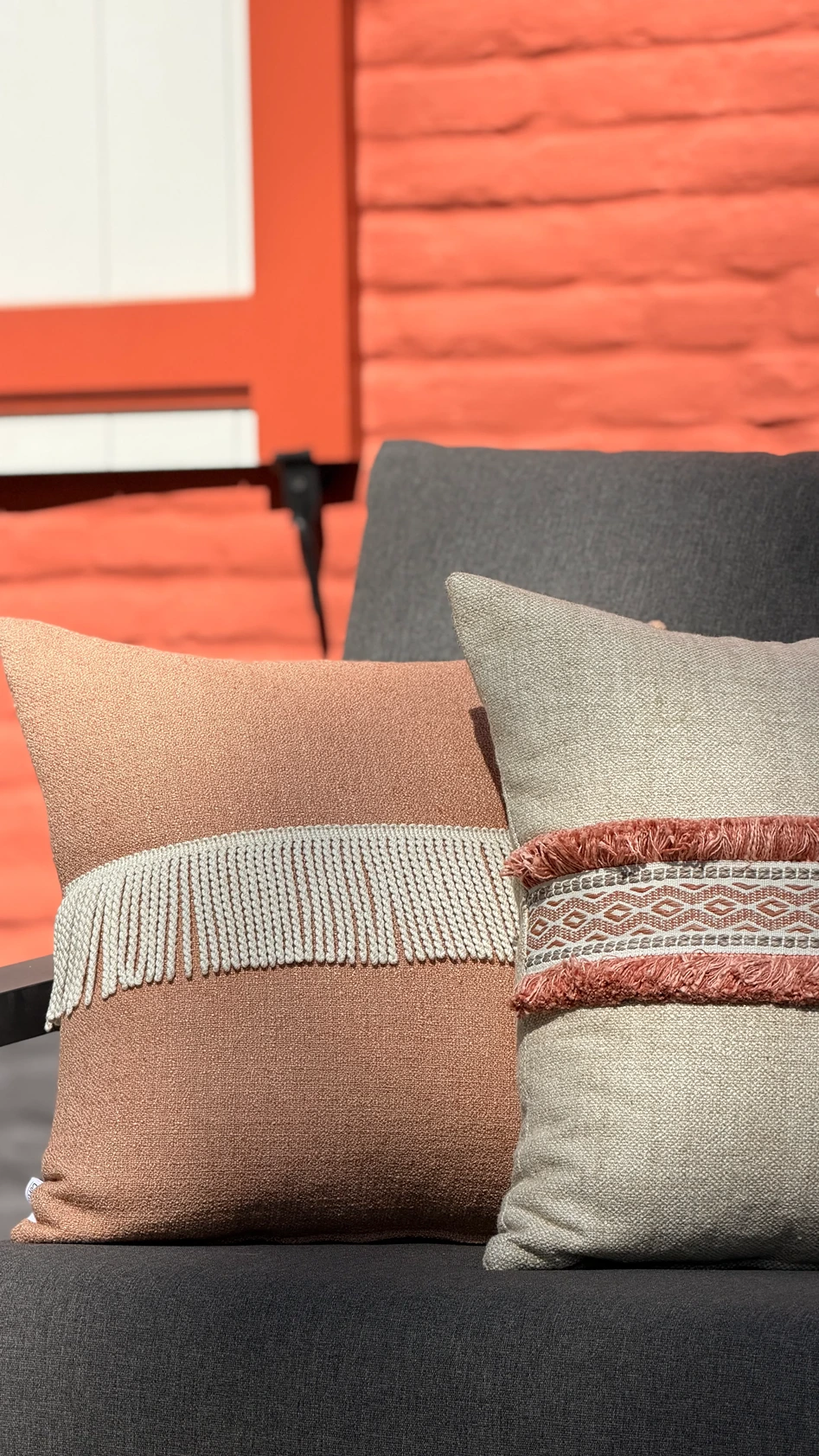 Buitensierkussens in terracotta met crèmekleurige franjerand en beige met boho-patroon op een antracietgrijze buitenbank