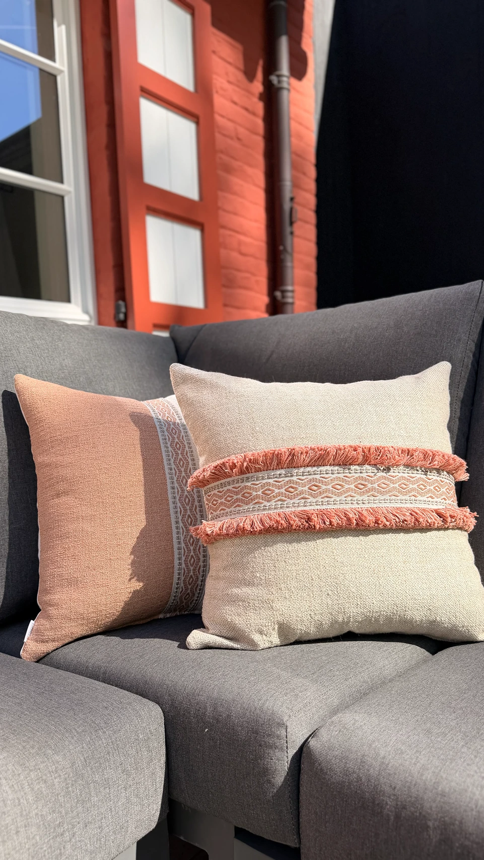 Buitensierkussens in terracotta en beige met franjes en boho-patroon op een antracietgrijze buitenbank