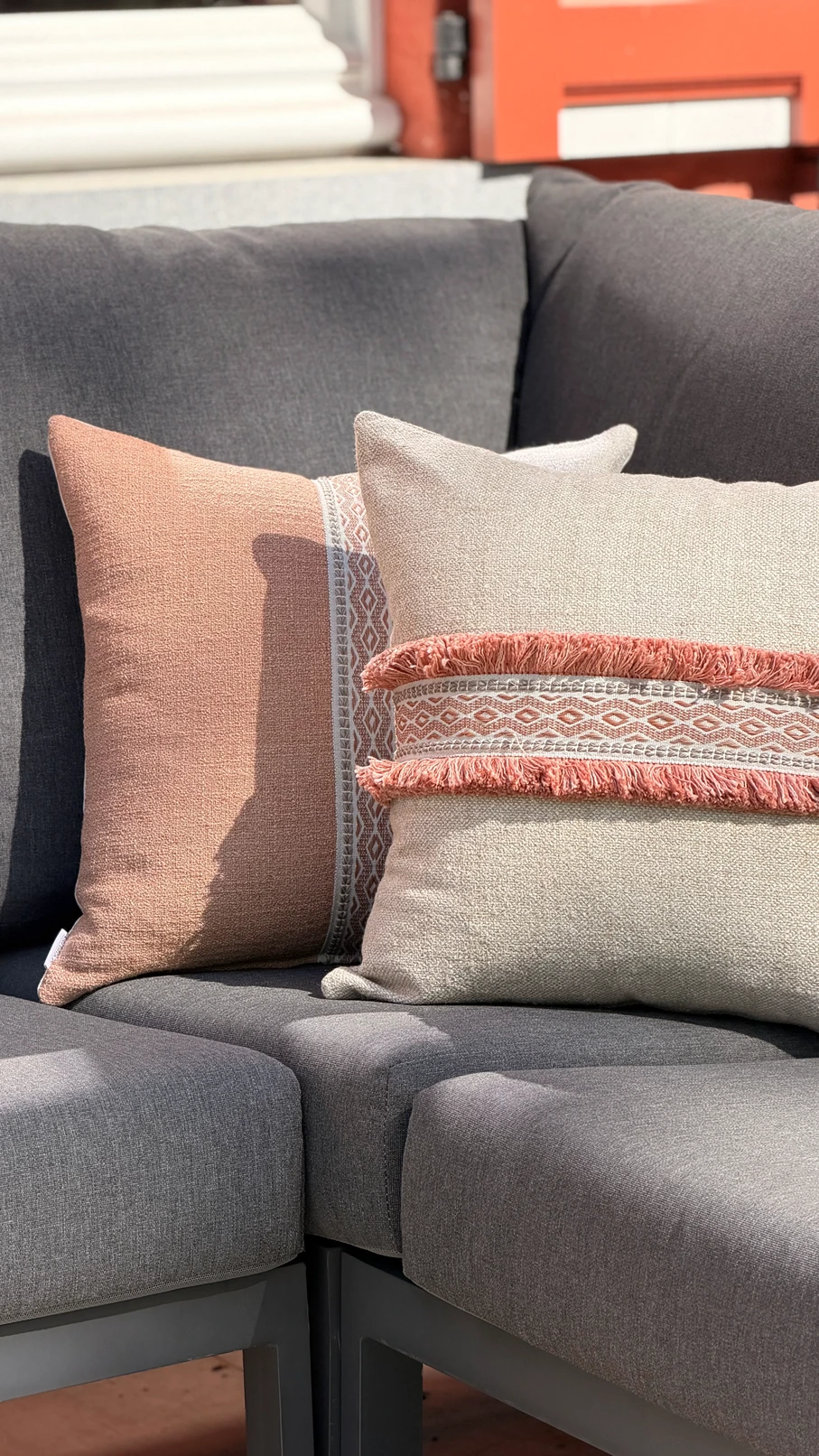 Buitensierkussens in terracotta en beige met franjes en boho-patroon op een antracietgrijze buitenbank