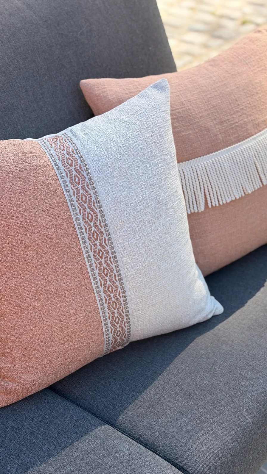 Buitensierkussens in terracotta en grijs met boho-patroon en franjerand op een antracietgrijze buitenbank
