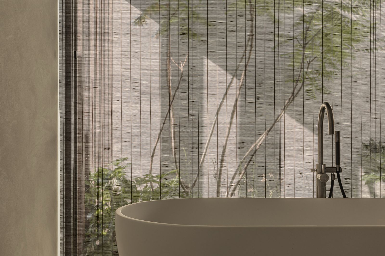 Vrijstaand bad voor een raam met transparant gesmokt zonweringdoek en zicht op een groene binnentuin