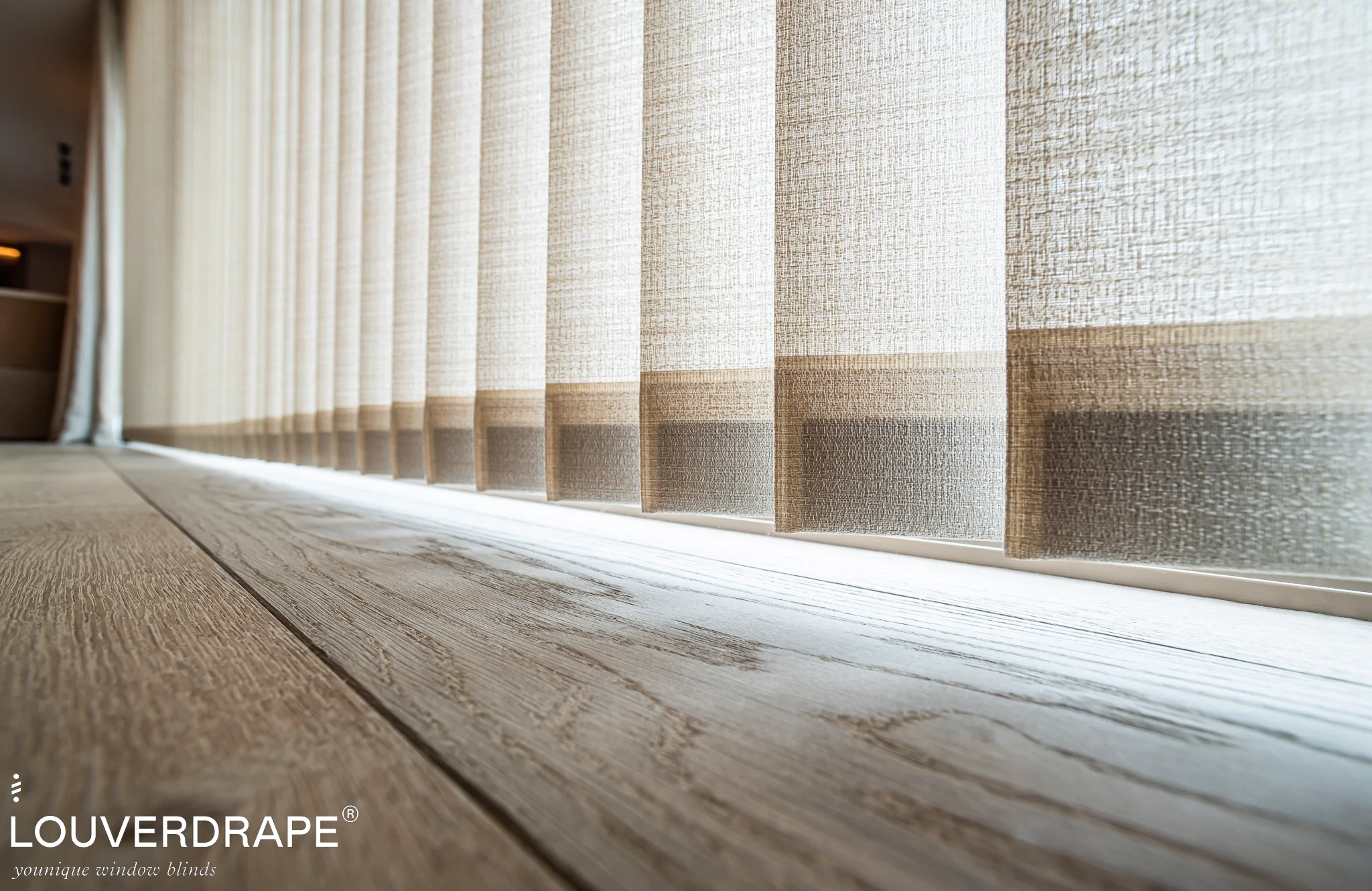 Close-up op vloerniveau van verticale lamellen van Louverdrape in wit met een gestreept patroon in taupe