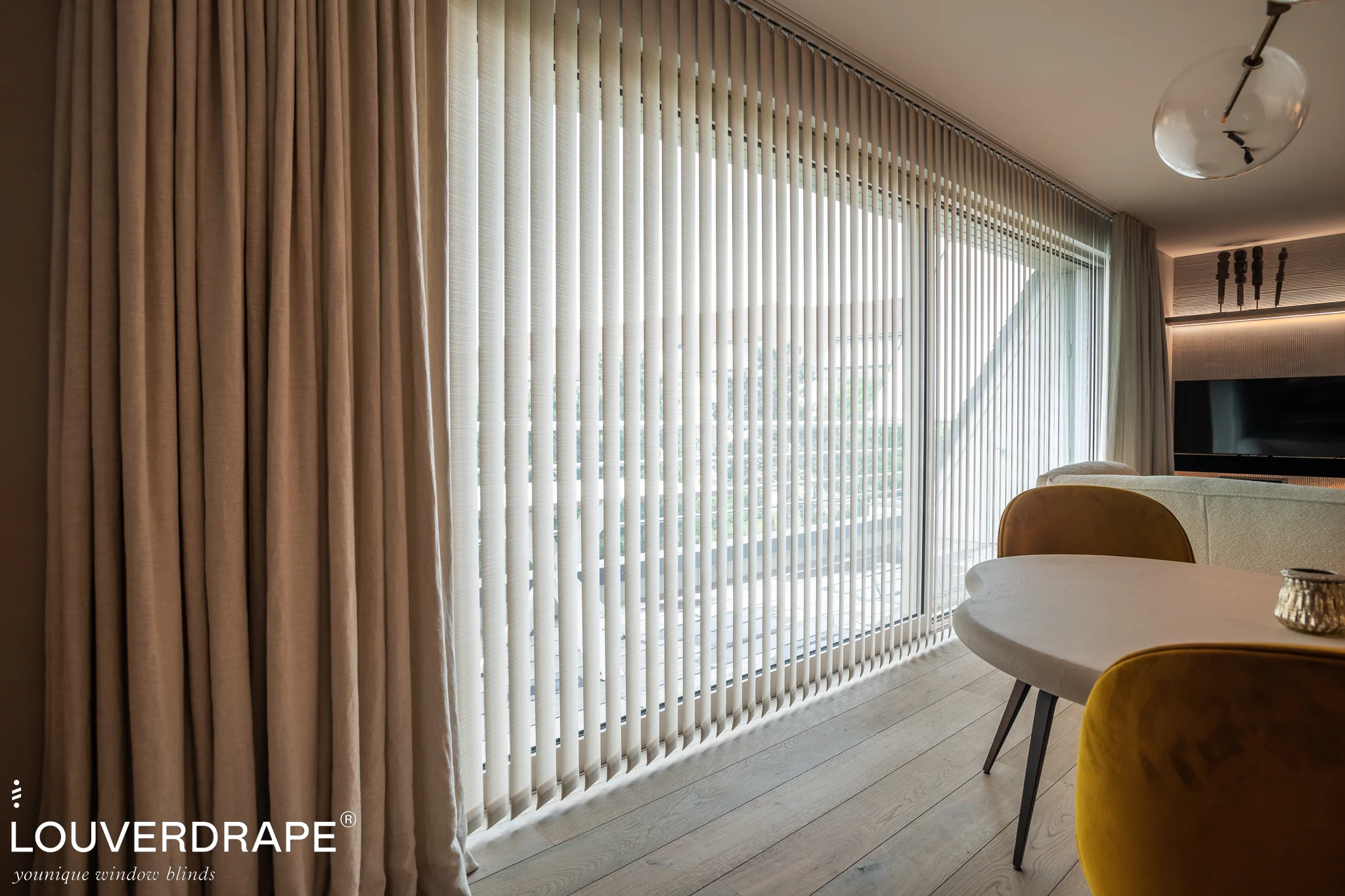 Witte verticale lamellen van Louverdrape voor een grote raampartij in een moderne woonkamer met beige gordijnen en gele stoel