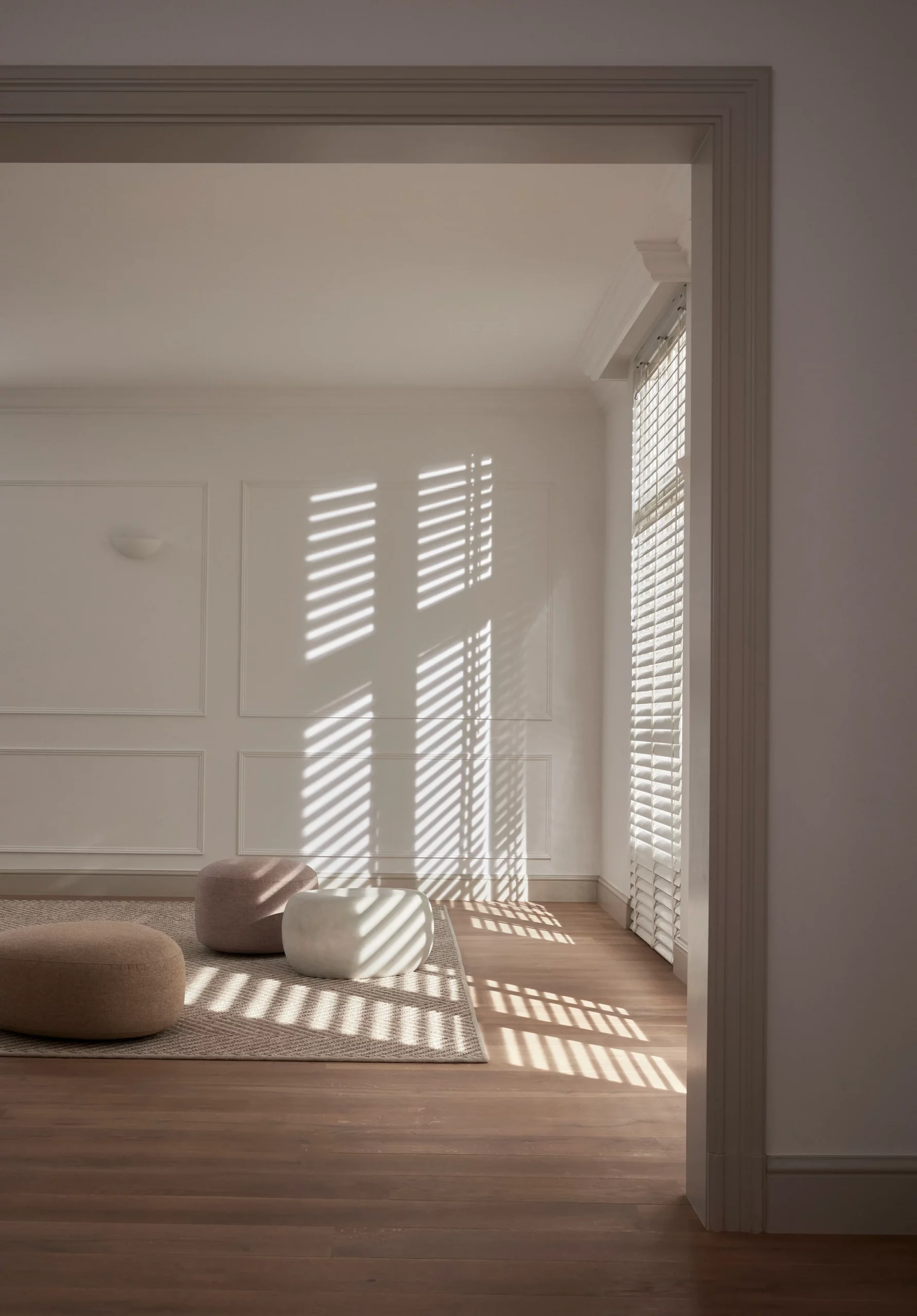 Witte jaloezieën met lijnenspel van licht en schaduw in een klassiek interieur met poefs op een tapijt