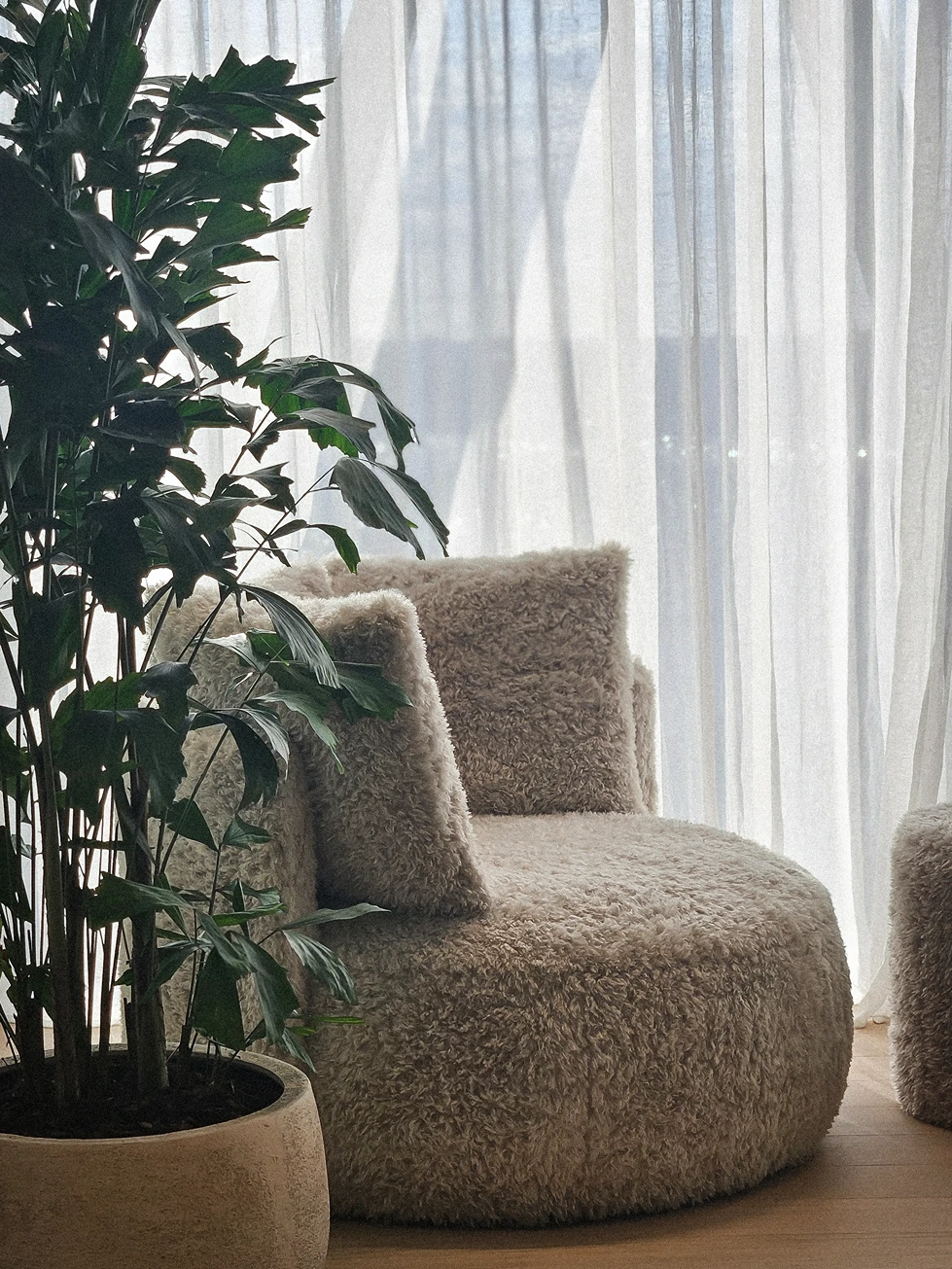Zachte wollige shaggy fauteuil voor een raam met wit vitragegordijn, naast een kamerplant